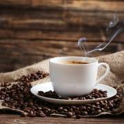 یک فنجان قهوه و دانه قهوه در کنار آن