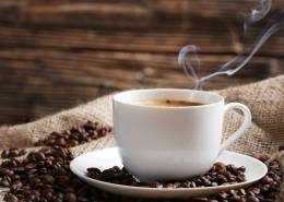 یک فنجان قهوه و دانه قهوه در کنار آن